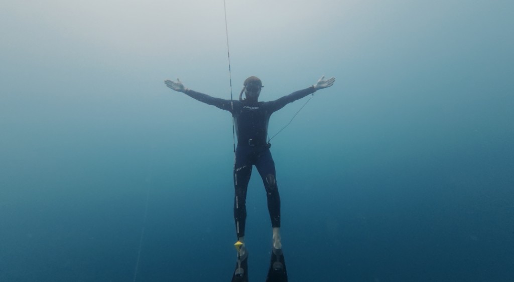 Freediver in open water with arms wide, on the line